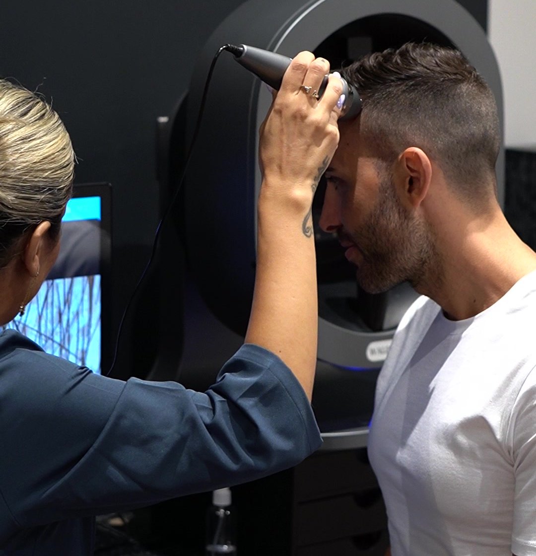 A Waldor Clinic hair and scalp restoration specialist running the AI scalp analysis probe across a client's hairline in London